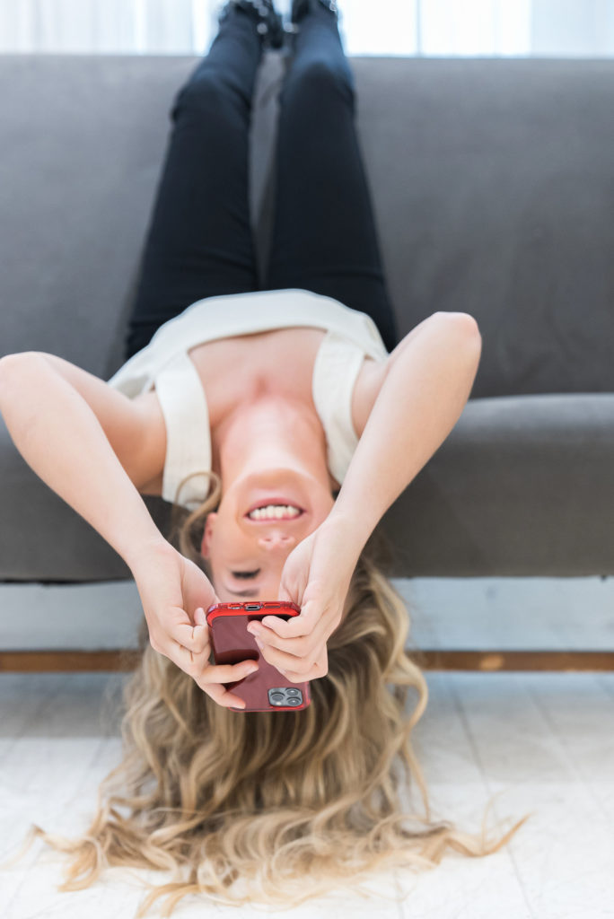 girl sitting upside down holding phone and smiling