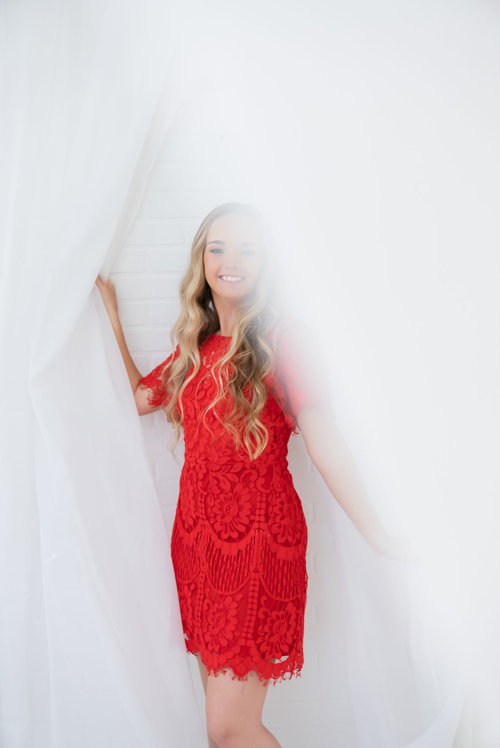 girl in red dress standing in curtains